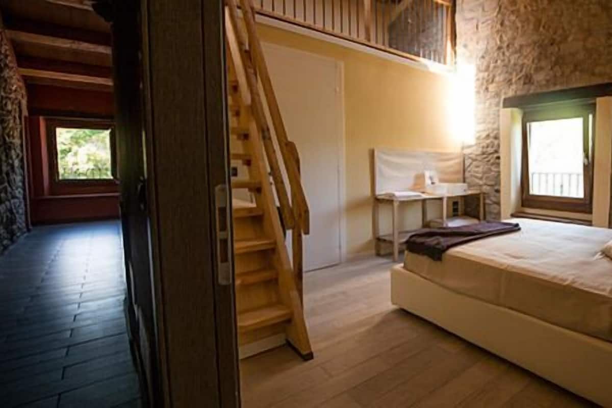 A bedroom with a wooden bed, a small desk, a chair, and a window.