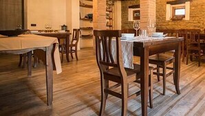 A dining area with wooden tables and chairs, a stone wall, and a sofa. - Brisighella Green Wellness (Brisighella)