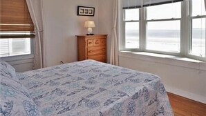 Une chambre à coucher avec un lit, une commode, une lampe et une fenêtre donnant sur la plage.