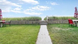 Un sentier qui mène à une plage, de part et d’autre, on y trouve des chaises et des parasols.