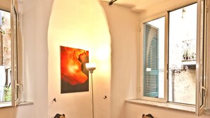 Um quarto com duas cadeiras, uma mesa, um abajur e uma janela grande.