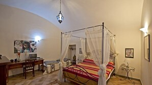 Um quarto com uma cama de dossel, uma escrivaninha com cadeira, uma televisão e uma mesinha de cabeceira com abajur.