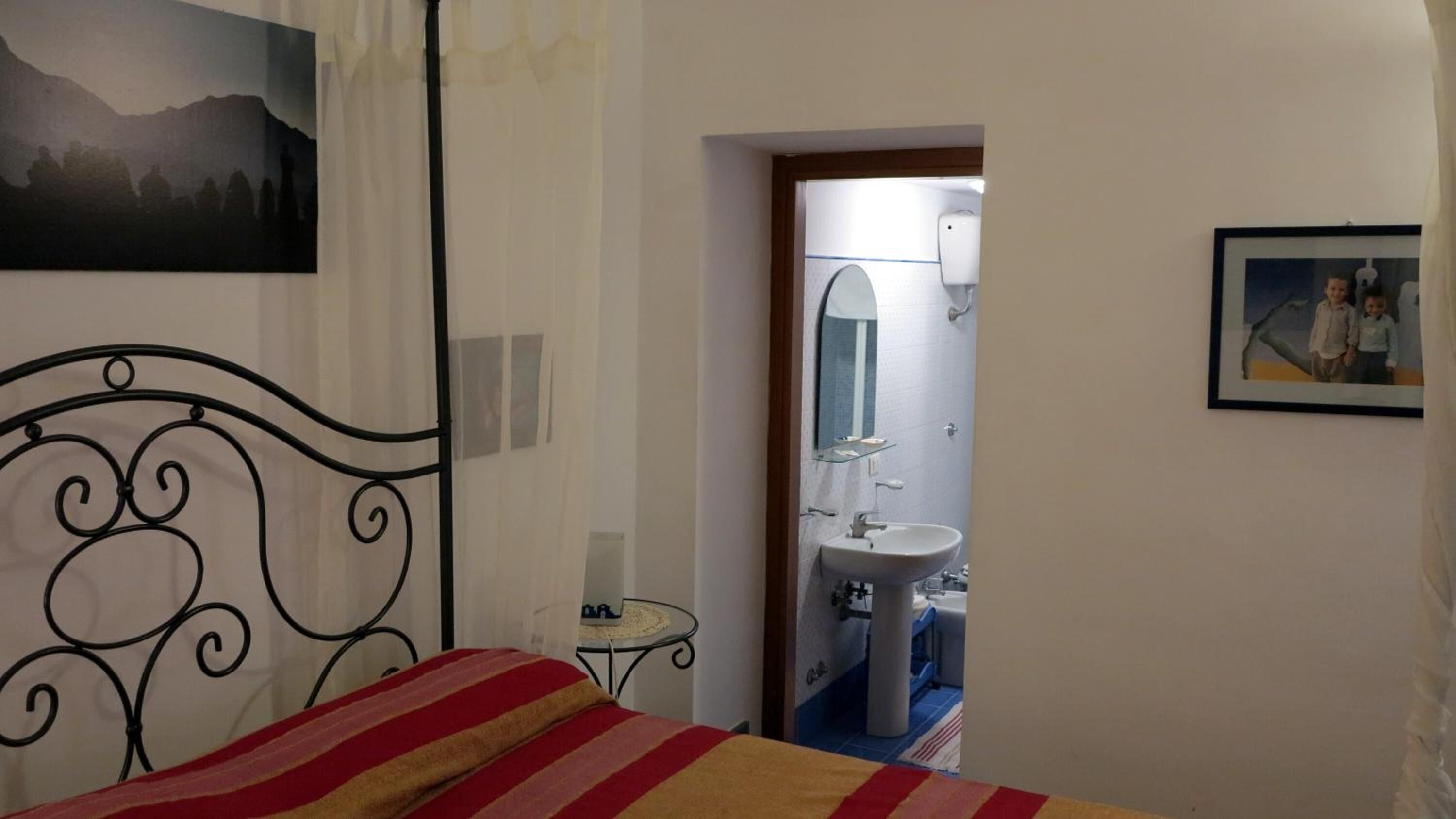 A bedroom with a bed, a bedside table, a mirror, and a bathroom visible through an open door.