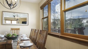 Une salle à manger avec une table en bois dressée pour quatre personnes, un lustre et une grande fenêtre donnant sur un paysage enneigé.