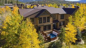 Une grande maison à deux étages, dotée d’un jacuzzi dans le jardin, entourée d’arbres aux couleurs automnales et avec des montagnes en toile de fond.