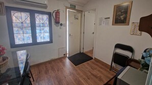 A room with a wooden floor, a glass table, a chair, a door, and a wall-mounted air conditioner.