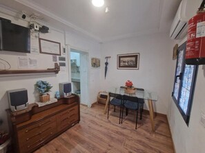 A room with a wooden floor, a TV, a fireplace, a dining table with chairs, and a window with a view.