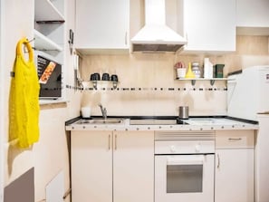 A compact kitchen with white cabinets, a built-in oven, a sink, and a stove.