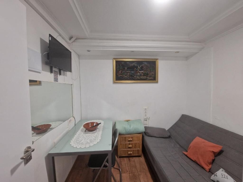 Una habitación pequeña con una mesa, un sofá, un televisor y un cuadro en la pared.