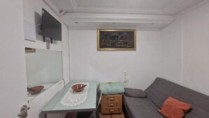 A small room with a table, a sofa, a television, and a painting on the wall.