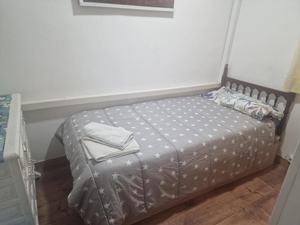 A single bed with a star-patterned bedspread, a wooden headboard, and a white wall with a framed picture above it.