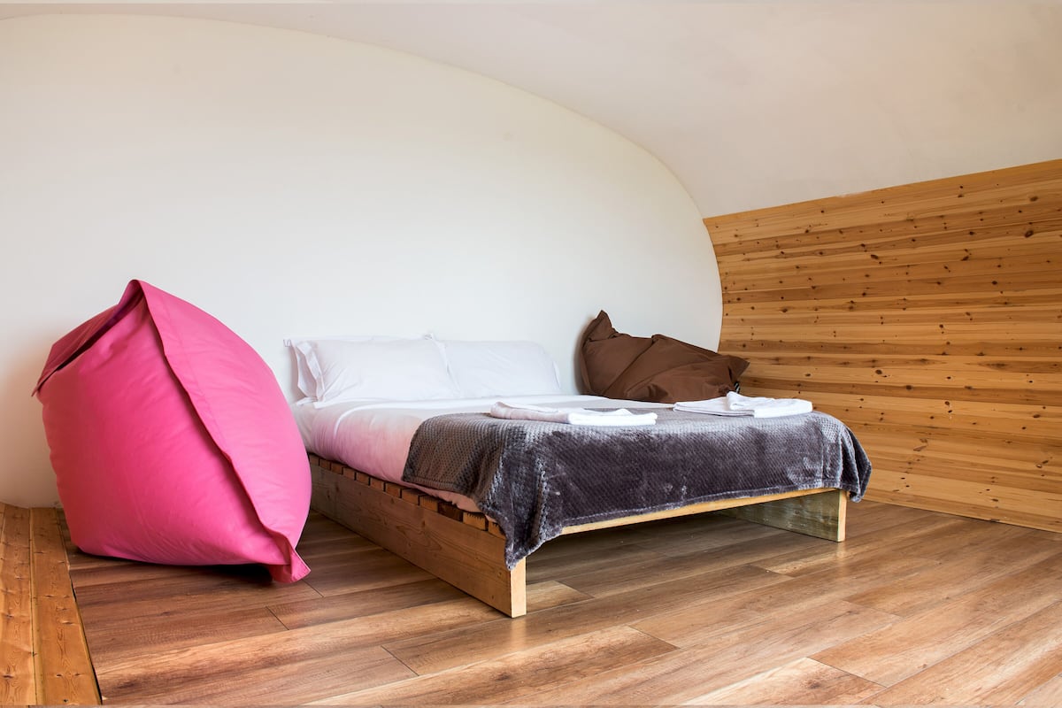 A bed with a wooden frame, a pink bean bag, and a brown pillow.