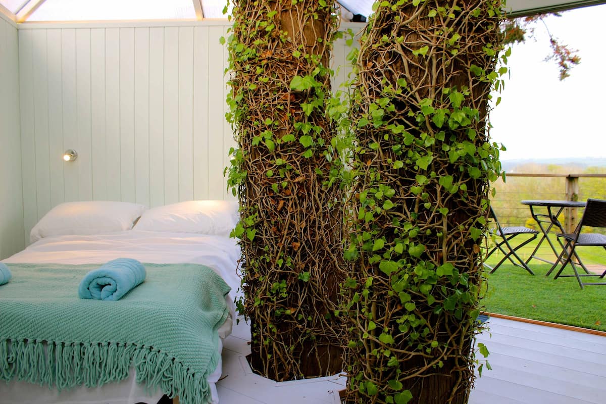 A bedroom with a bed, a green blanket, and a wall covered in ivy.