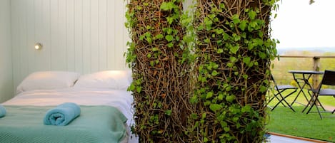 A bedroom with a bed, a green blanket, and a wall covered in ivy.