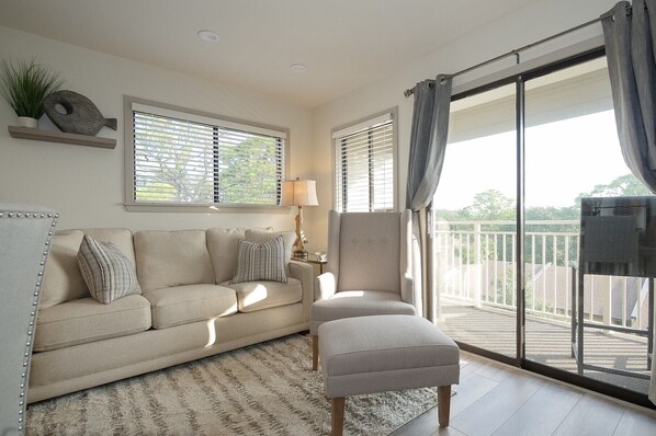 A living room with a sofa, a chair, a lamp, and a large window with blinds. - Great Ocean views, Oceanfront Heated Pool! (Hilton Head)
