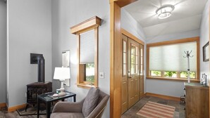 Ein Zimmer mit Kamin, einem Tisch mit Lampe, einem Stuhl, Holztüren und einem Fenster mit Jalousien.