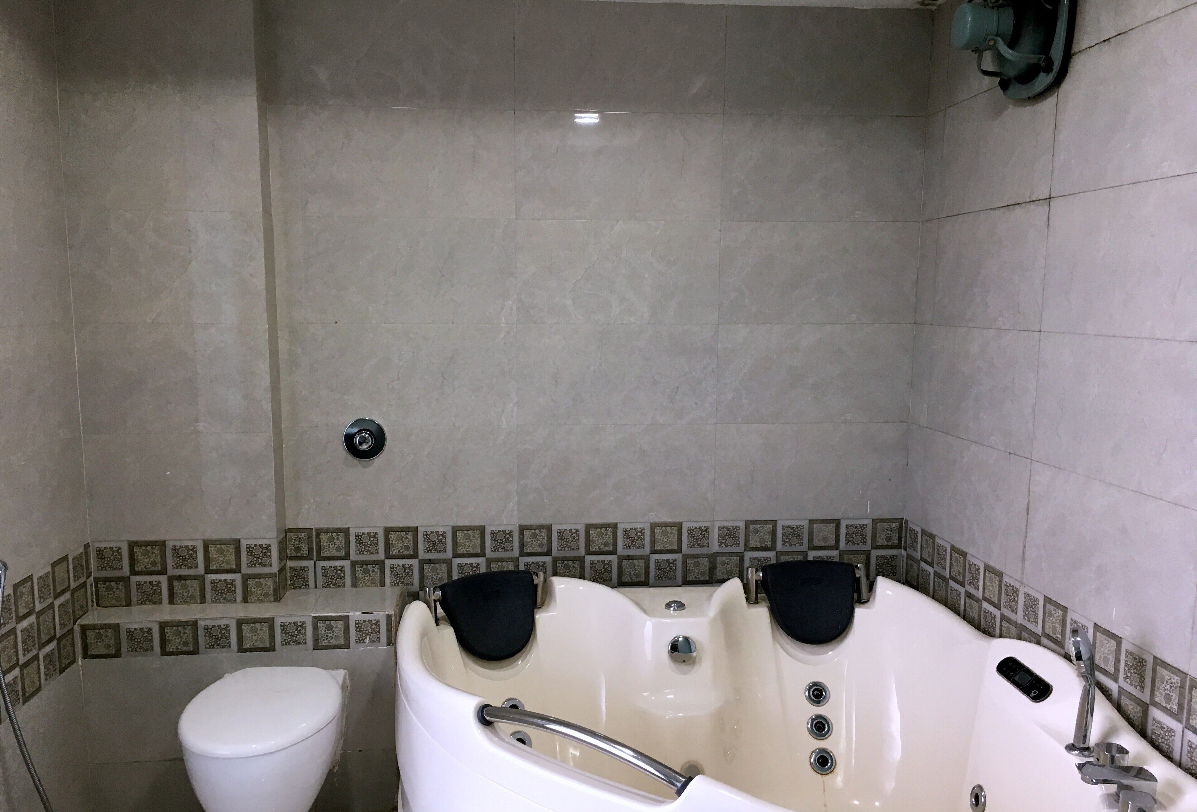 Een badkamer met een badkuip, twee zwarte badzitjes, een toilet en betegelde wanden.
