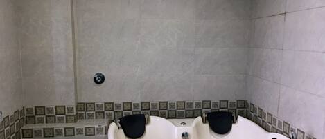 A bathroom with a bathtub, two black bath seats, a toilet, and tiled walls.