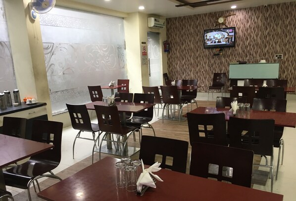 A restaurant with multiple tables and chairs, a television mounted on the wall, and a patterned wall.