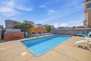 A rectangular swimming pool with a wooden deck, surrounded by lounge chairs and a hot tub.