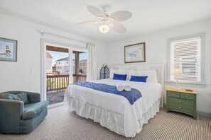 A bedroom with a bed, a chair, a nightstand, a ceiling fan, and a window with blinds.
