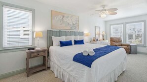 Une chambre à coucher avec un lit, des lampes de chevet, une chaise, un ventilateur de plafond et un tableau au mur.