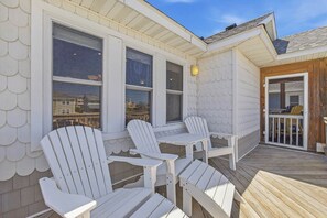 Eine überdachte Terrasse mit Adirondack-Stühlen und einem Holgittergeländer.