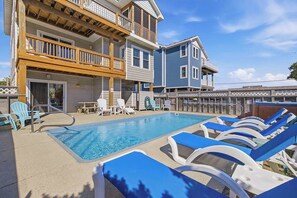 A pool area with lounge chairs, a wooden deck, and a two-story building with balconies.