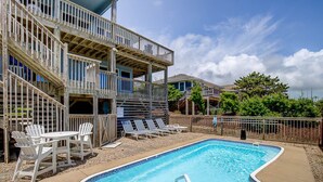 A pool area with a wooden deck, lounge chairs, and a two-story building with balconies. - Dancing Dolphin | 240 ft from the beach | Private Pool, Hot Tub, Dog Friendly | Duck (Duck)