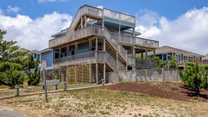 A multi-story building with a wooden exterior and a balcony on the upper floor. - Dancing Dolphin | 240 ft from the beach | Private Pool, Hot Tub, Dog Friendly | Duck (Duck)