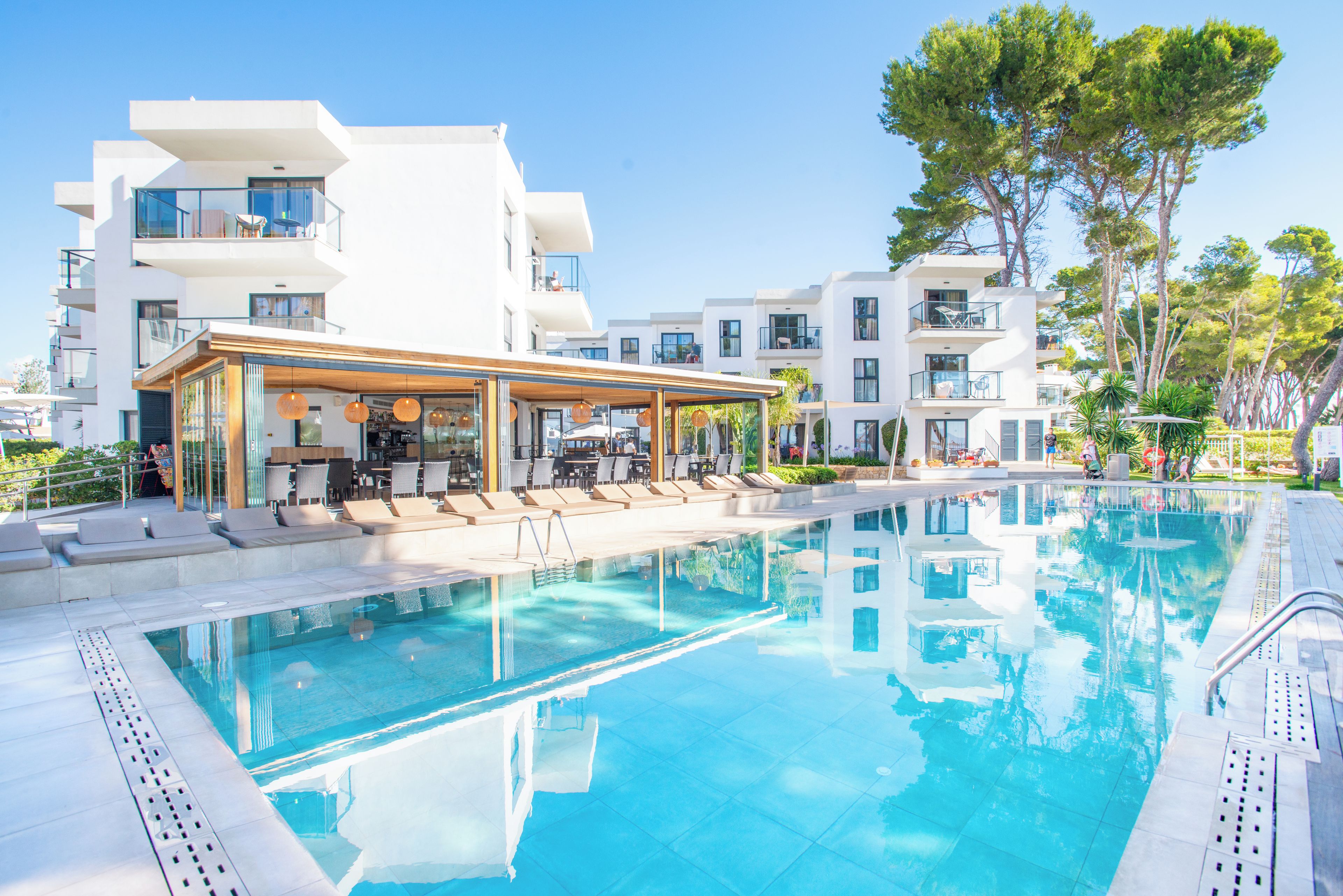 A modern hotel with a swimming pool, outdoor seating, and a covered area with umbrellas.
