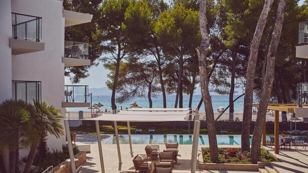 Un espace aménagé au bord de la piscine, avec des sièges extérieurs, une vue sur la mer et un bâtiment doté de balcons.