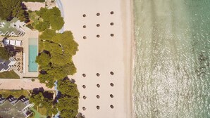 Vue aérienne d’une propriété située sur la côte, avec une plage, une piscine et un groupe d’arbres.