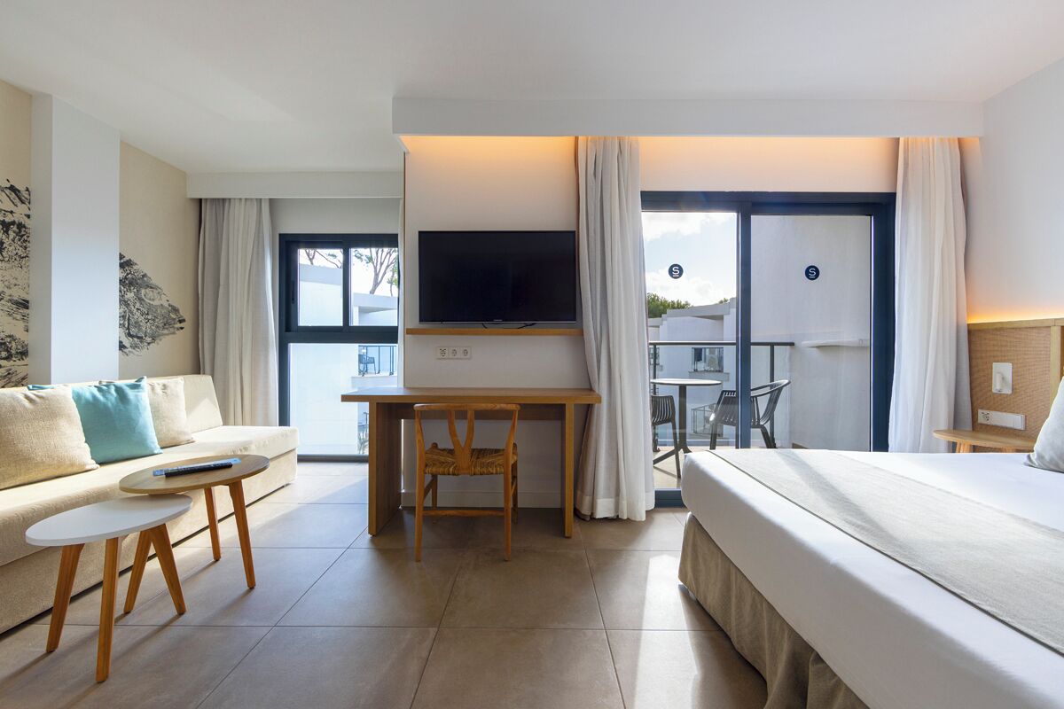 Una habitación de hotel moderna con cama, escritorio con televisor, una mesita pequeña y un sofá.