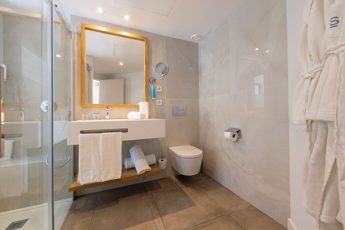 A modern bathroom with a glass shower enclosure, a wooden vanity, a toilet, and a large mirror.