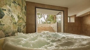 Un espace bien-être comprenant un jacuzzi, un mur en pierre et un escalier menant à l’extérieur.