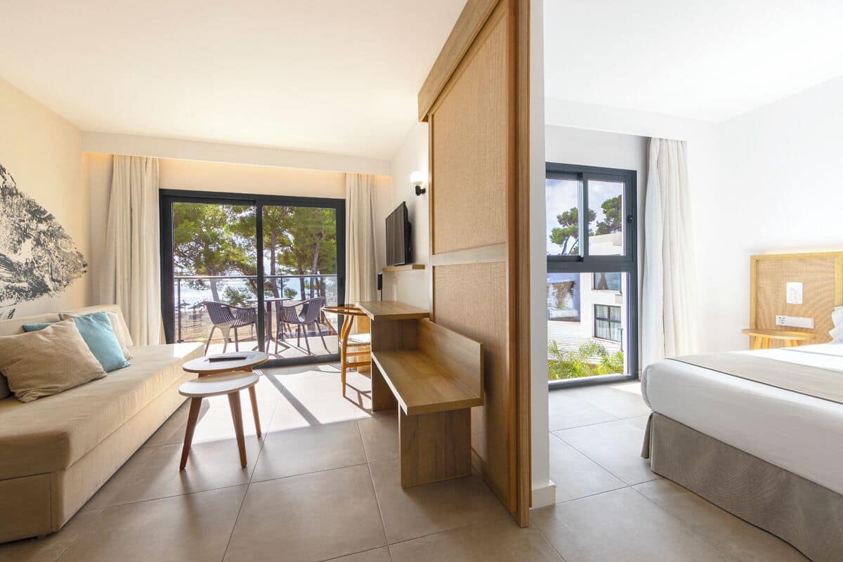 Quarto de hotel moderno com sofá, uma mesinha, cama e varanda com vista para a cidade.