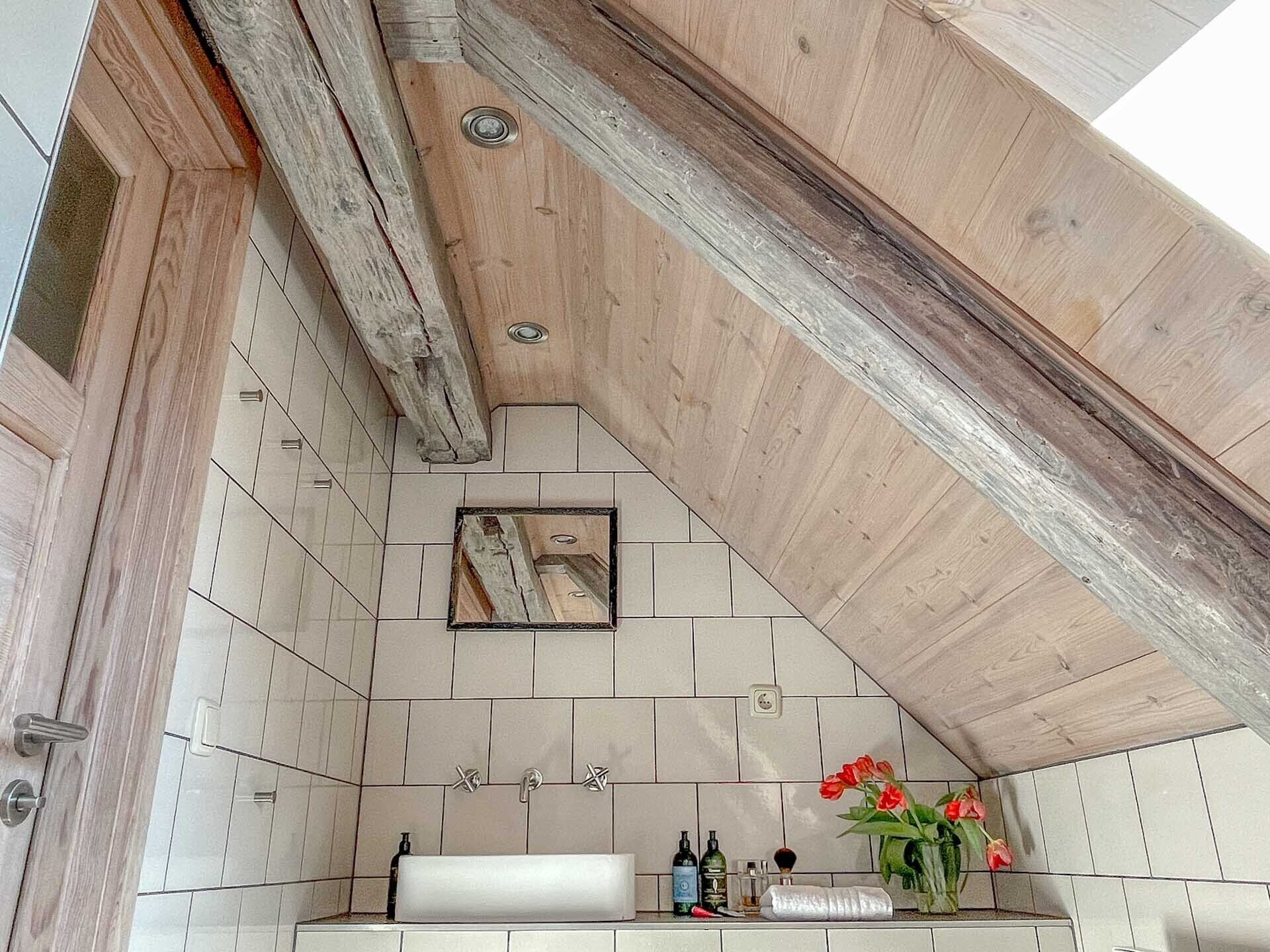 A bathroom with wooden beams, a tiled wall, a sink, and a mirror.