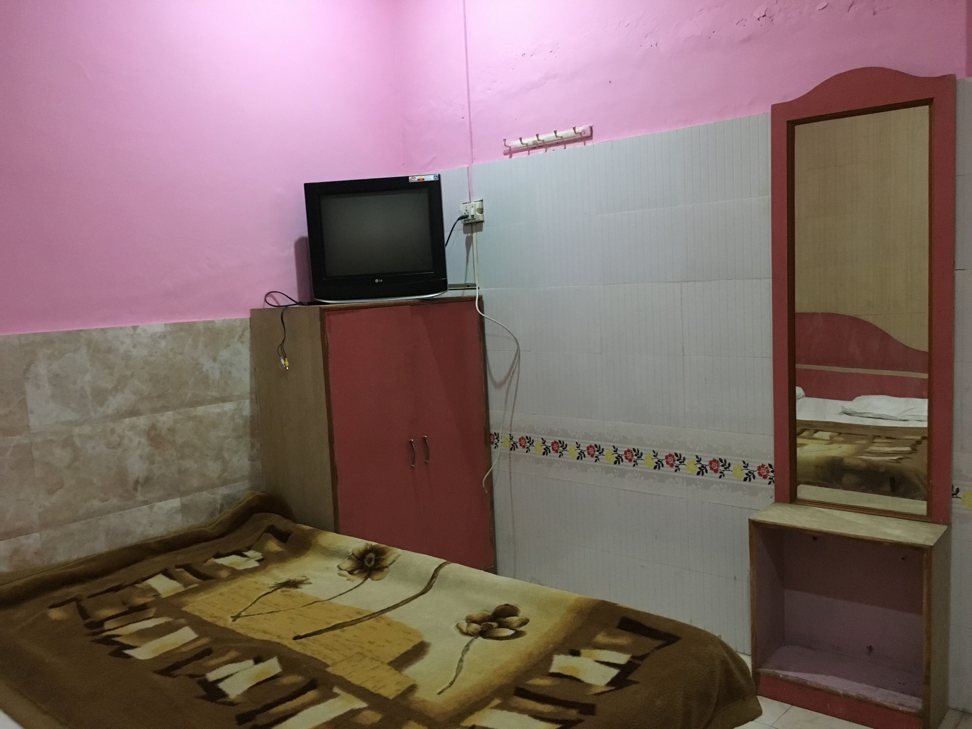 Quarto com cama, televisão sobre um móvel, espelho e guarda-roupa.