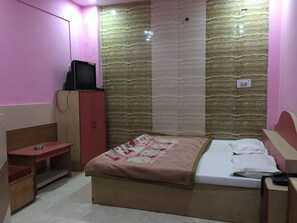 A bedroom with a bed, a TV on a stand, a wardrobe, and a small table. - Hotel Bundelkhand Palace (Lalitpur)