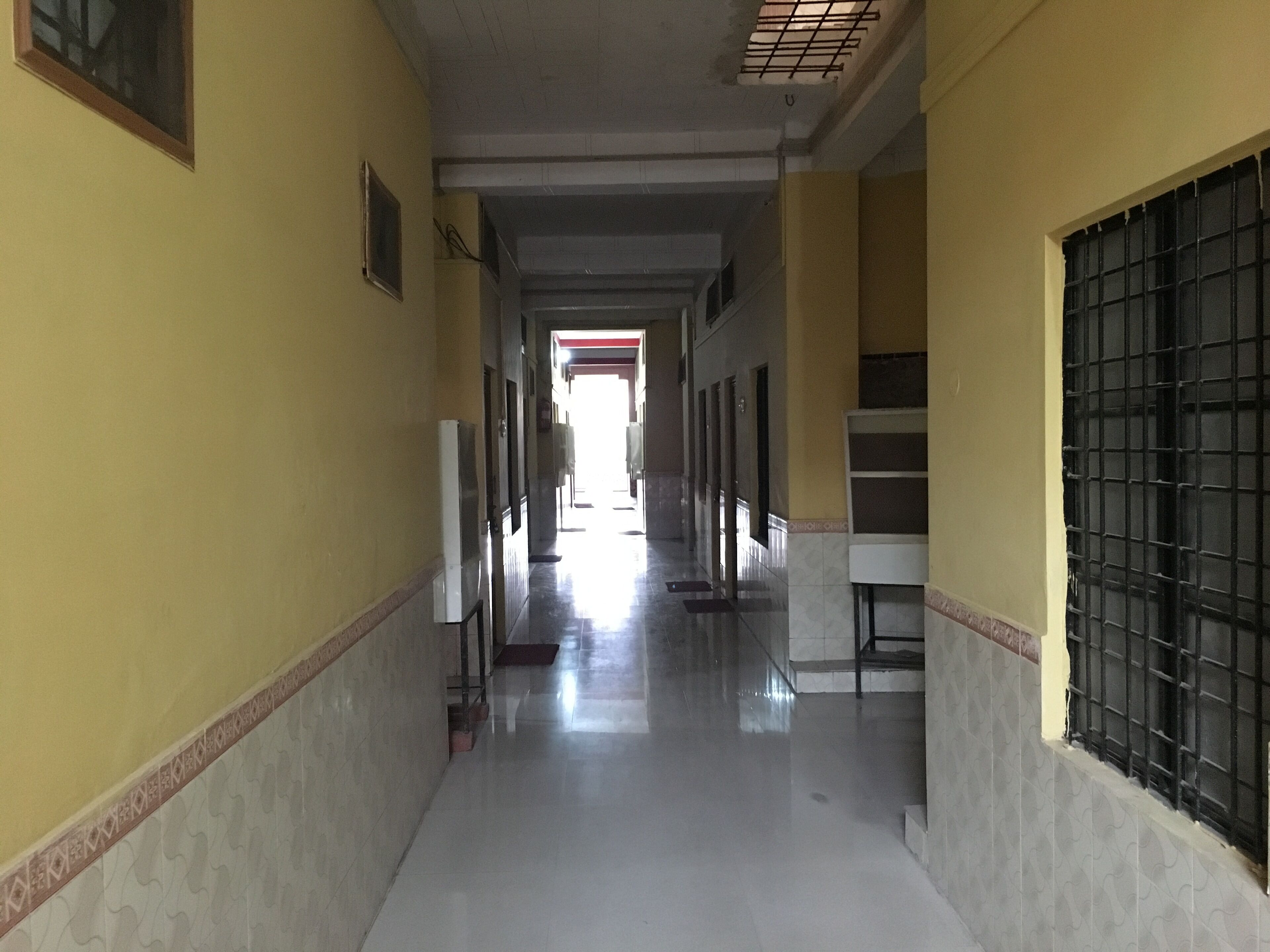 A long, narrow hallway with tiled walls and a shiny floor, leading to a bright exit.
