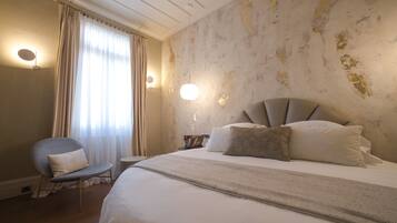 Habitación de hotel con una cama grande, una silla, una mesita de noche y una lámpara de pared.