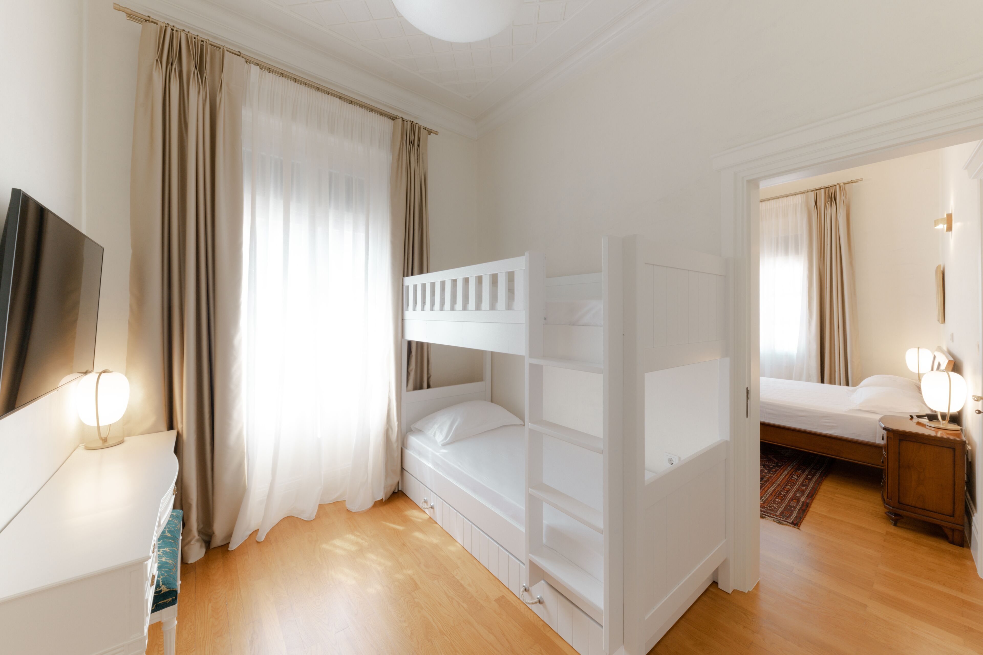 A room with a bunk bed, a bedside table with a lamp, a wardrobe, and a mirror.