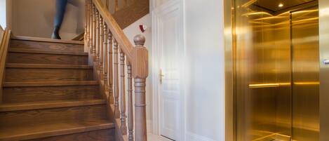 A wooden staircase with a handrail, a black and white checkered floor, and a gold elevator.