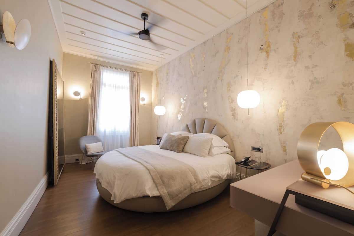 A modern bedroom with a round bed, a bedside table, a chair, and a ceiling fan.