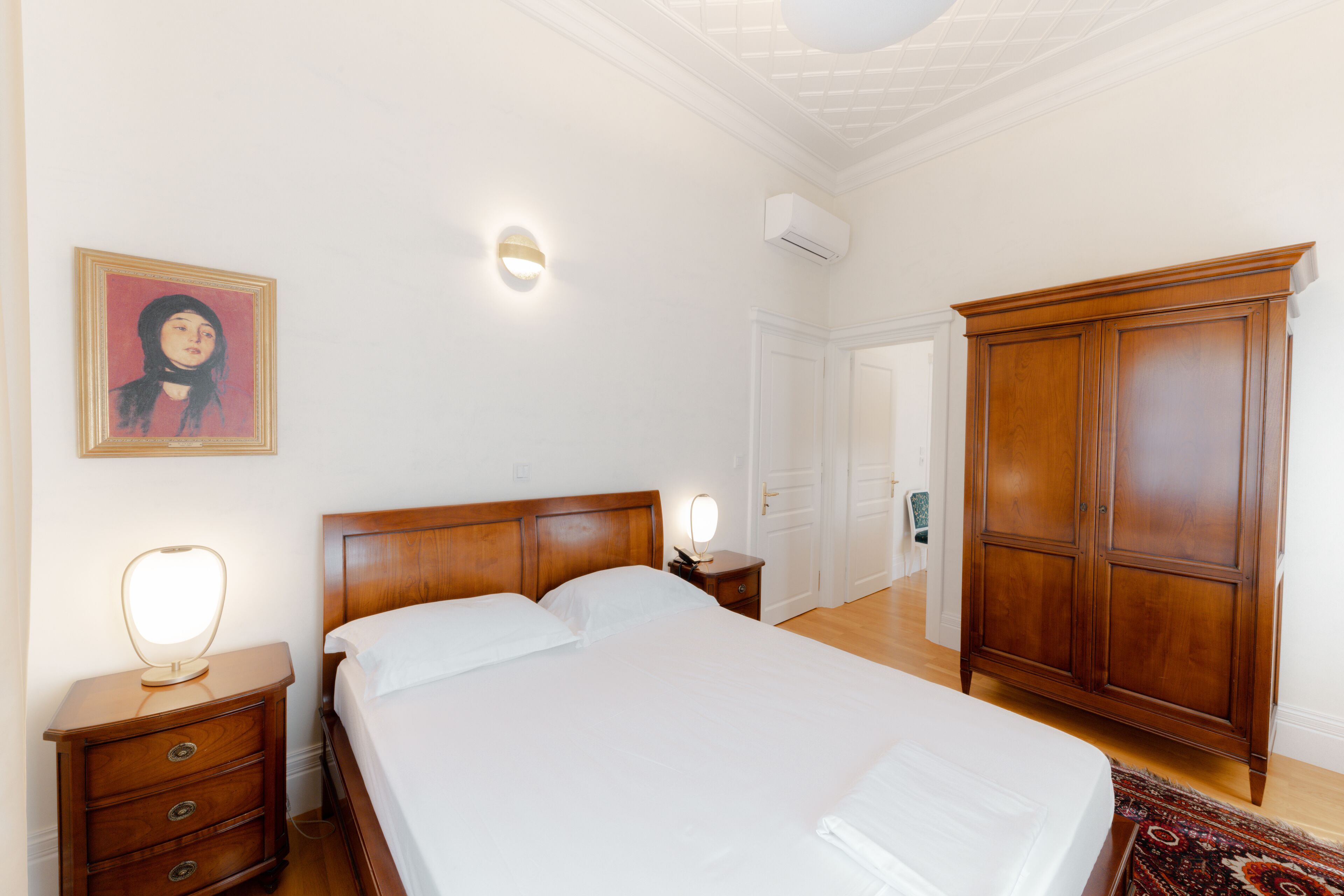 Une chambre à coucher avec un lit en bois, des tables de chevet, une armoire et un luminaire fixé au mur.