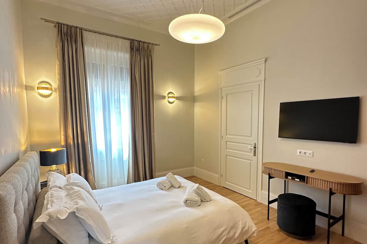 A hotel room with a bed, a desk, a TV, and a window with curtains.