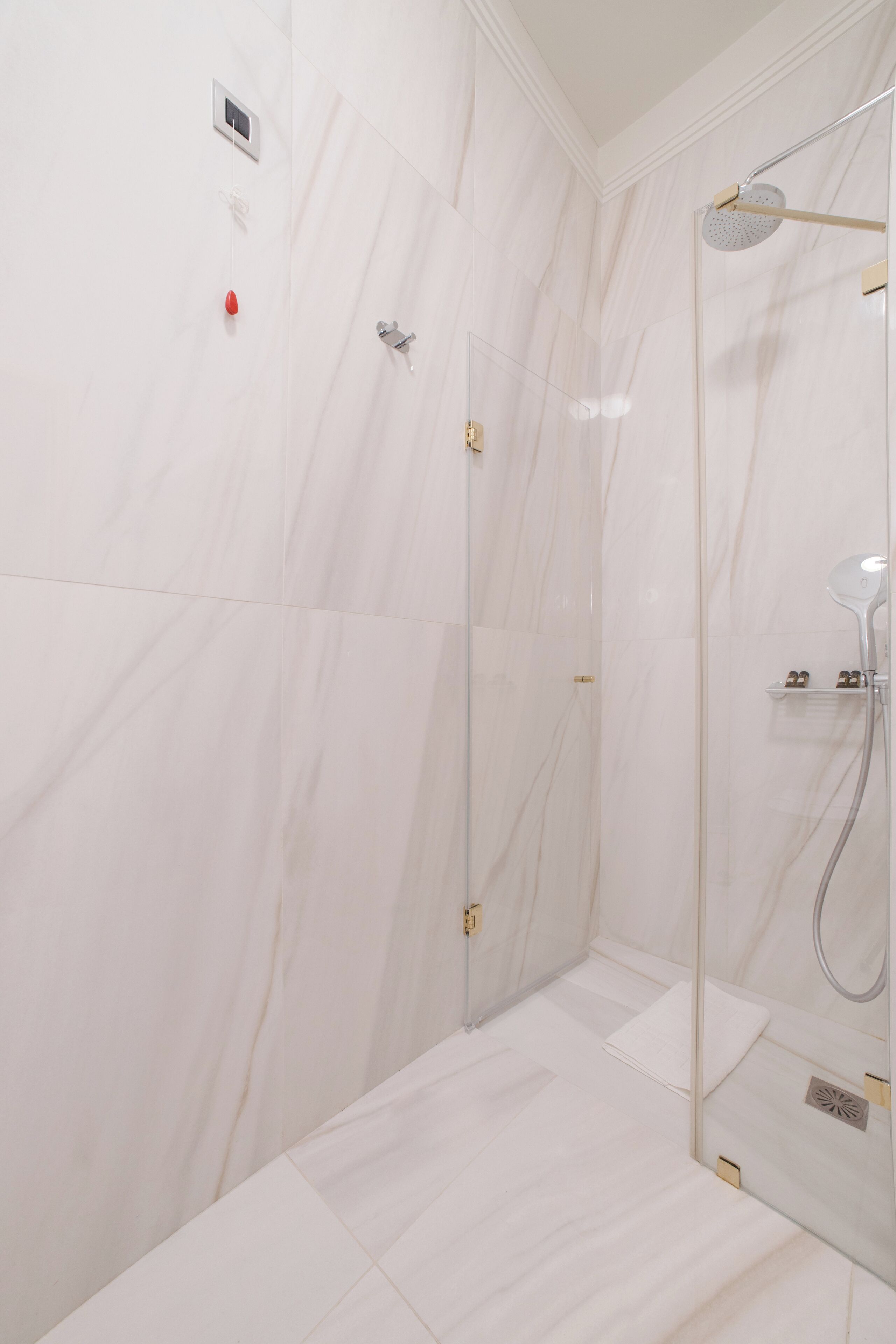 A modern bathroom with white marble tiles, a glass shower enclosure, and a visible control panel.