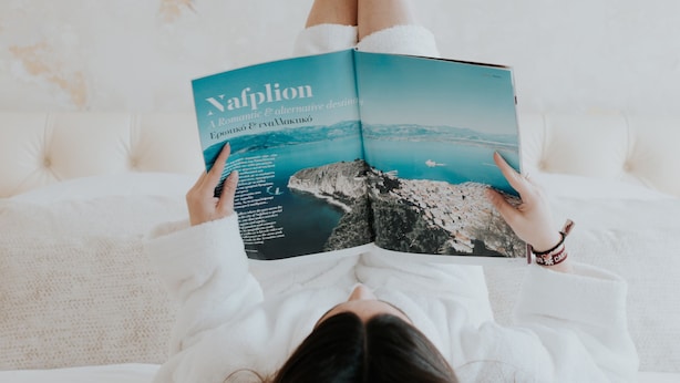 Eine Person liegt auf einem Bett, vor ihr liegt ein Buch mit dem Titel 'Nafplion'.