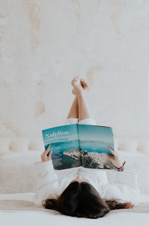 A person lying on a bed with a book titled 'Nafplion' in front of them. - Castellano Hotel & Suites (Nafplio)